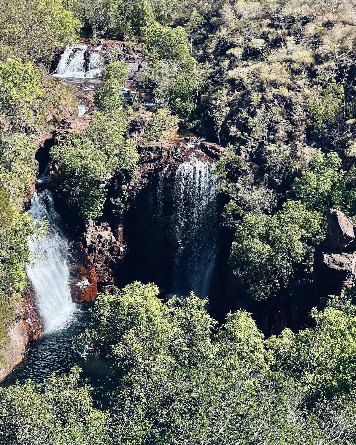 Twin waterfalls of Florence Falls pour into a shaded plunge pool surrounded by dense green monsoon forest in Litchfield
