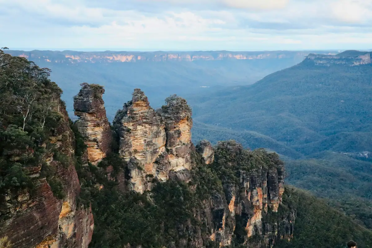 The Three Sisters sandstone pillars rise from forested cliffs above the hazy blue Jamison Valley