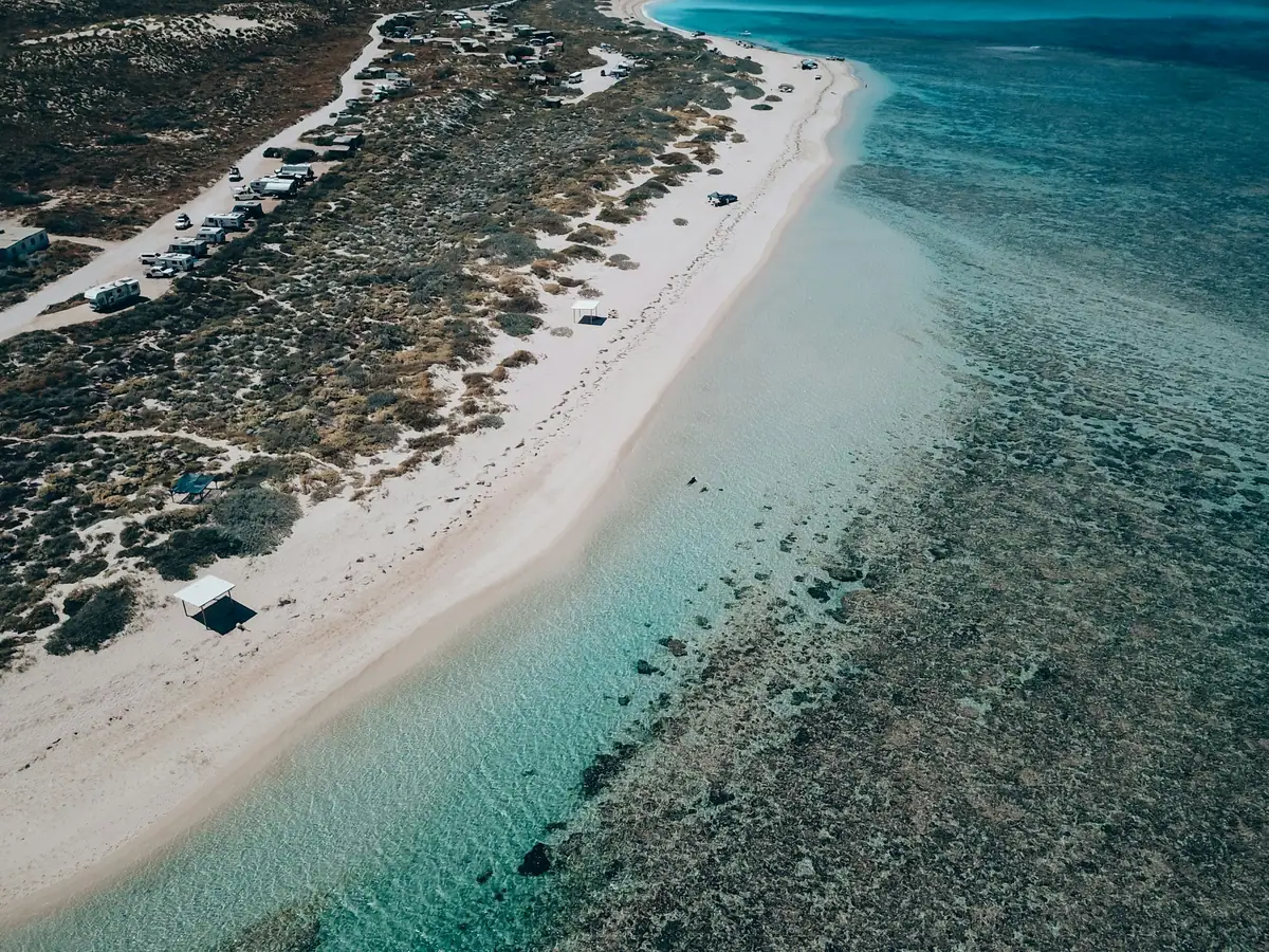 Aerial of a white sand point and shallow clear water over reef at Coral Bay